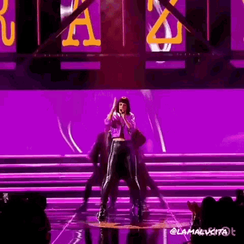 a woman singing into a microphone on a stage with purple lights behind her