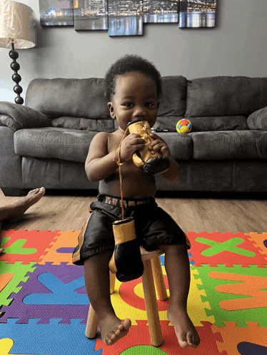 a baby wearing boxing gloves is sitting on a stool in front of a couch