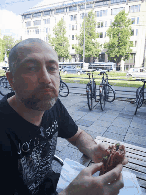 a man wearing a shirt that says joy division is eating a sandwich