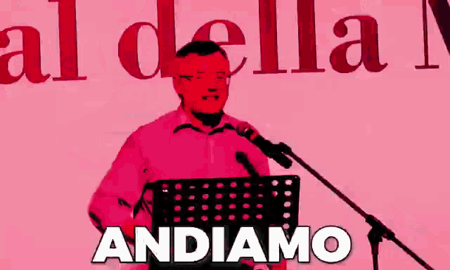 a man in a red shirt stands in front of a microphone with the word andiamo written below him
