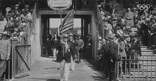 a black and white photo of a man holding an american flag in front of a crowd