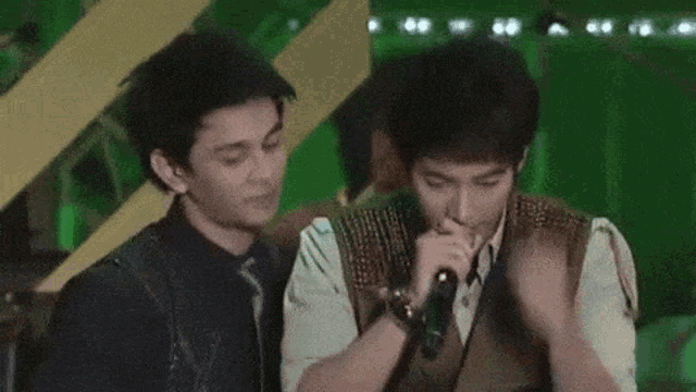two young men are standing next to each other and one of them is holding a microphone in his mouth .