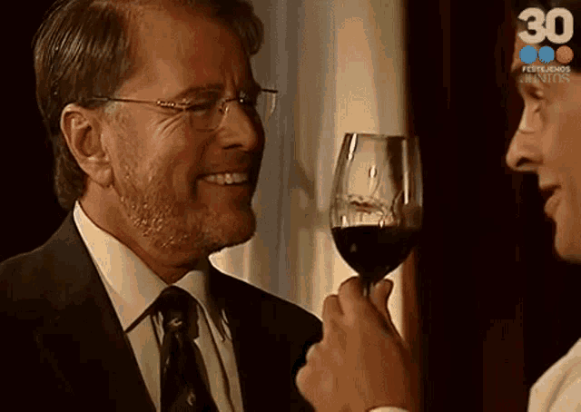a man in a suit and tie is holding a glass of wine and smiling