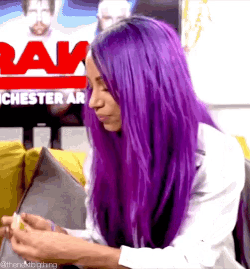 a woman with purple hair is sitting on a couch in front of a sign that says raw
