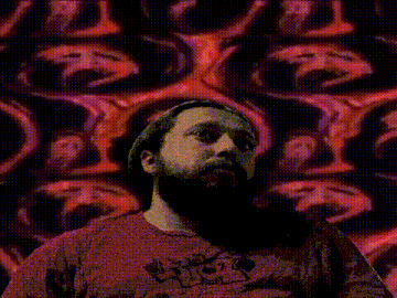 a man with a beard wearing a hat and a red shirt is standing in front of a wall with many faces .