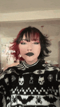 a woman with red hair and black lipstick is wearing a black and white sweater .