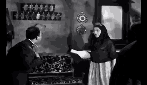 a man and a woman are standing in a living room talking to each other .
