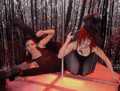 a woman with red hair is laying on a pole while another woman holds her legs up