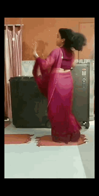 a woman in a pink saree is dancing in front of a refrigerator in a room .