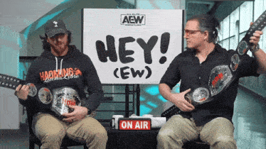 two men are sitting in front of a sign that says hey ew