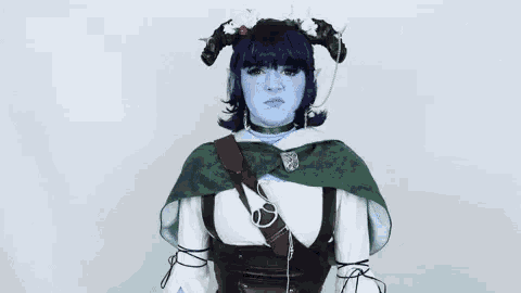 a woman in a cosplay costume with blue face paint and horns is holding a sword .