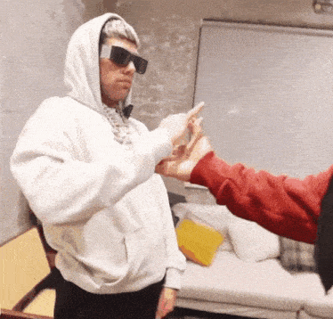 a man in a white hoodie and sunglasses is being pointed at by another man in a red shirt
