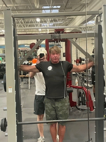 a man taking a picture of himself in a gym while wearing a t-shirt that says ' a '