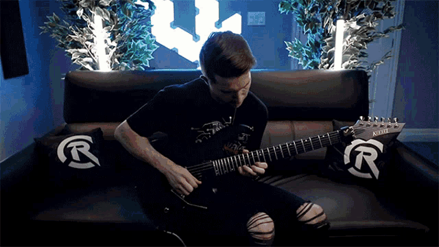 a man is sitting on a couch playing a guitar with a yamaha logo on the pillow