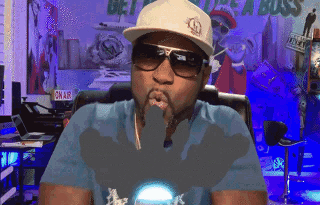 a man wearing a hat and sunglasses is sitting in front of a sign that says " on air "