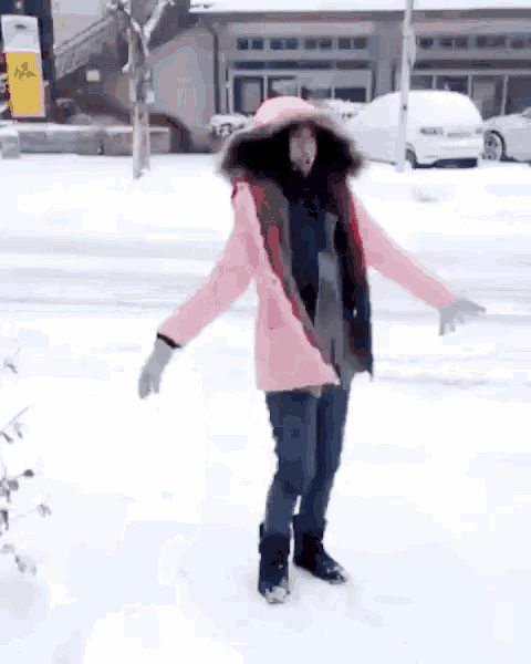 a woman in a pink coat stands in the snow with her arms outstretched