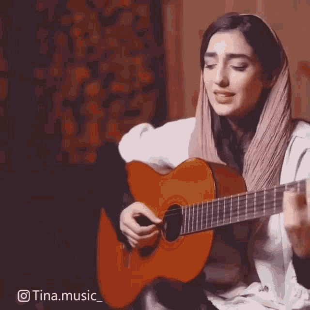a woman in a head scarf is playing a guitar .