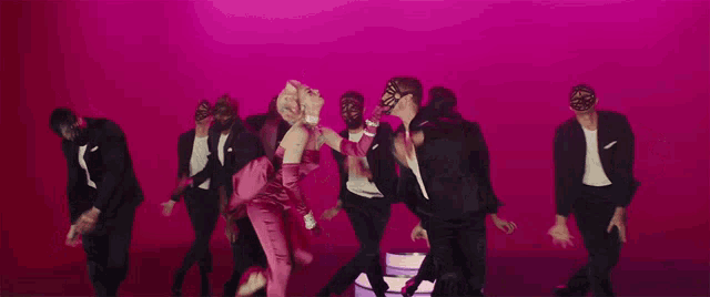 a woman in a pink dress is surrounded by men in black suits and masks