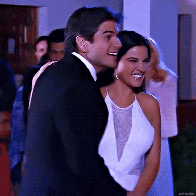 a man in a suit and a woman in a white dress are dancing together