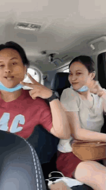 a man wearing a red shirt that says ac is giving a peace sign next to a woman wearing a mask