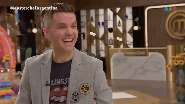 a man in a suit and a rolling stones shirt is smiling in front of a masterchef argentina sign