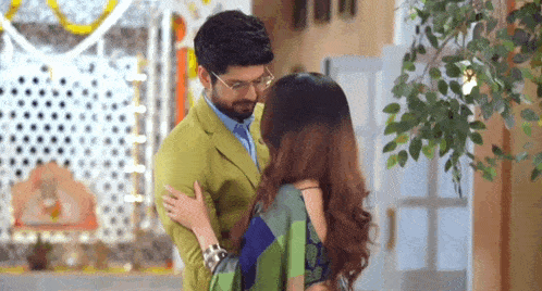 a man and a woman are standing next to each other in a room . the man is wearing a green suit .