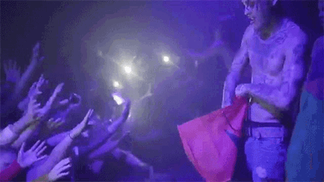 a man without a shirt is standing in front of a crowd of people at a concert .