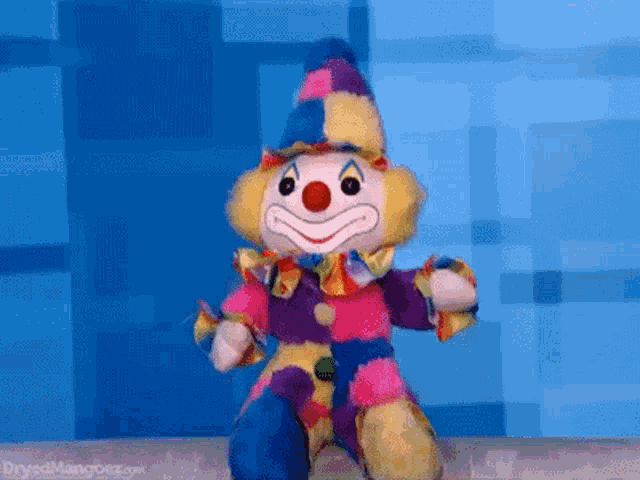 a stuffed clown is sitting on a table in front of a blue wall ..