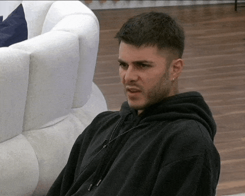 a man in a black hoodie sits in front of a couch