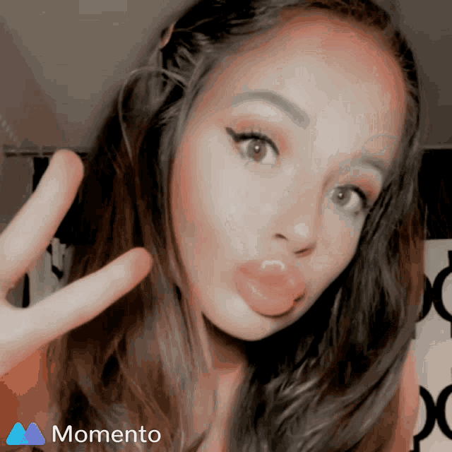 a woman making a peace sign with a momento logo in the background