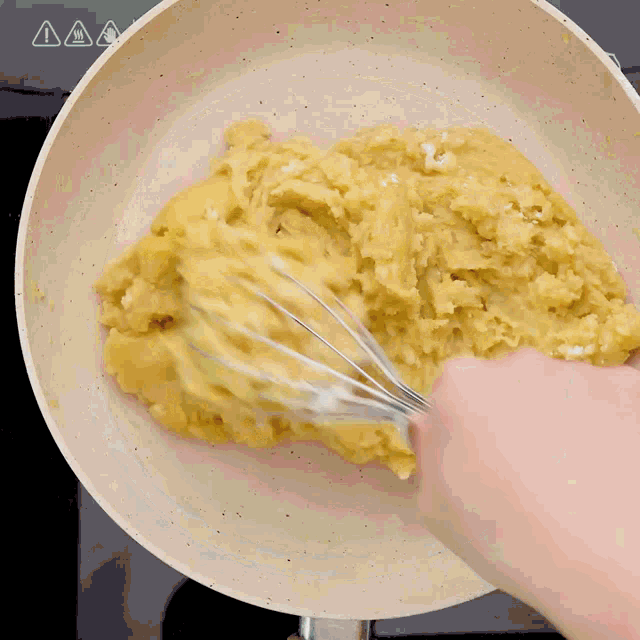 a person is whisking something in a pan with a warning sign above it
