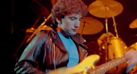 a man in a leather jacket is playing a guitar on a stage