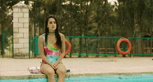 a woman in a bikini is sitting on the edge of a swimming pool .