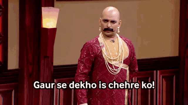 a bald man with a mustache is wearing a red dress and pearls and says gaur se dekho is chehre ko