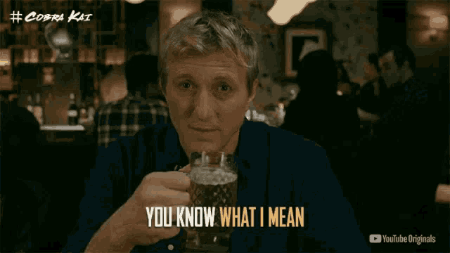 a man in a blue shirt is holding a glass of beer and says you know what i mean