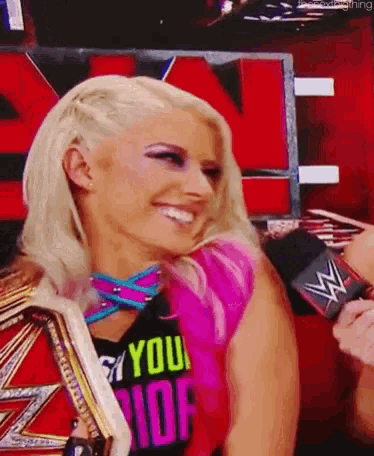 a woman wearing a shirt that says " you ride " is smiling and holding a wrestling championship belt .