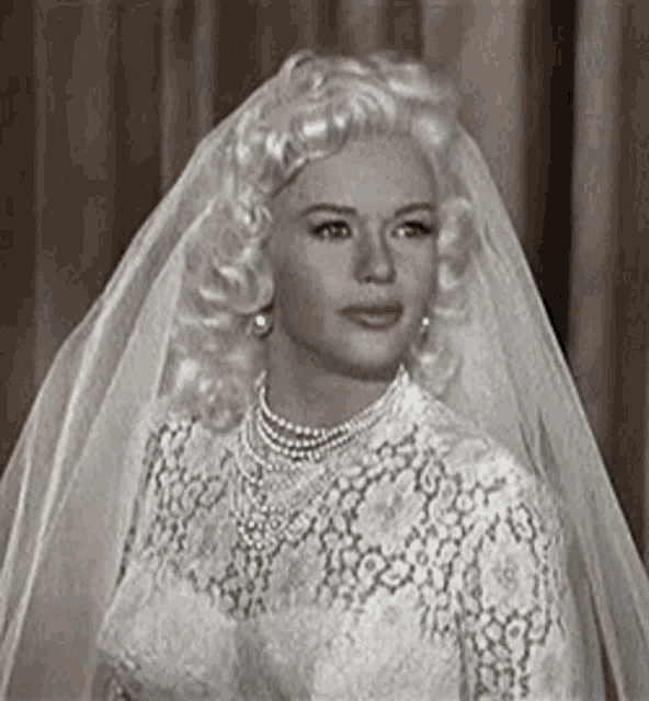 a woman in a wedding dress and veil is looking at the camera .