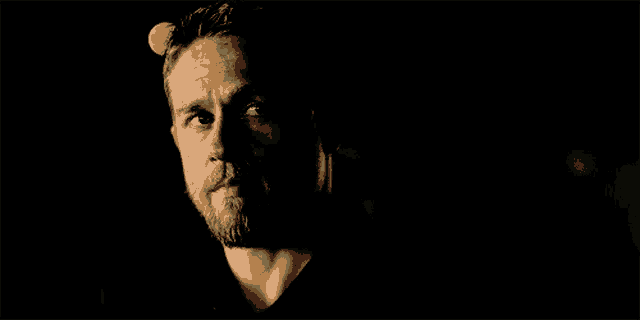a man with a beard is looking at the camera in the dark