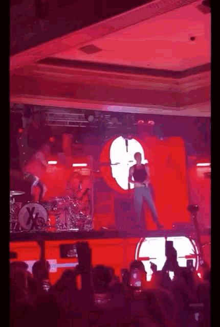 a man is standing on a stage in front of a x on a drum set