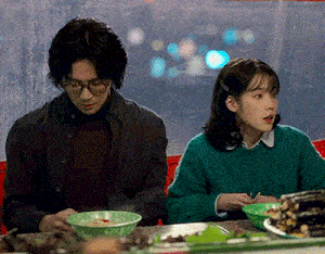 a man and a woman are sitting at a table eating food from bowls .