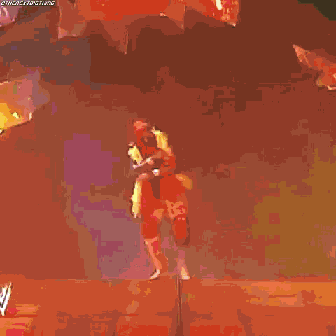 a wrestler in a red and yellow outfit is standing on a stage with his arm in the air .
