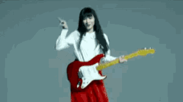 a woman in a red dress is playing a red electric guitar .
