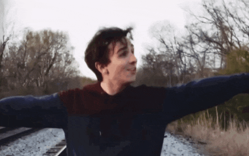 a young man with his arms outstretched is standing on train tracks