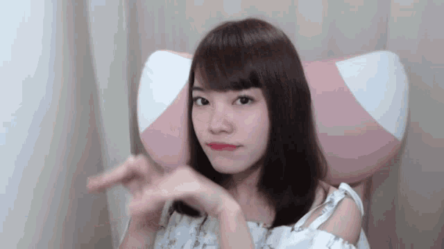 a young girl sitting in a pink chair making a heart shape with her hands