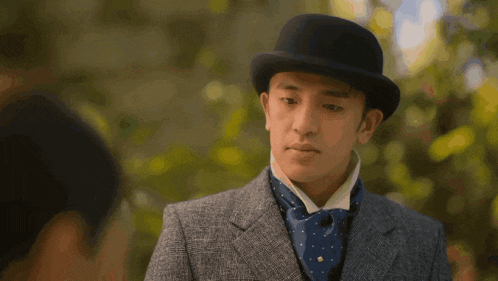a man wearing a suit and a bowler hat looks at another man