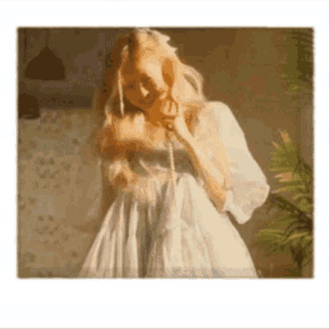 a woman in a white dress is talking on a telephone in a room .