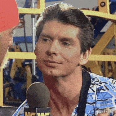a man is talking into a microphone and smiling while wearing a blue shirt .