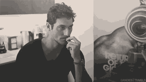 a man with a mustache is sitting in front of a camera and smoking a cigarette .