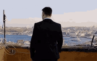 a man in a suit is standing on a balcony overlooking the ocean