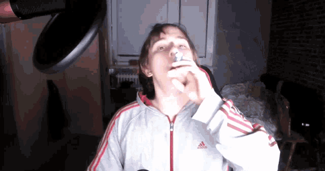a man wearing an adidas jacket is blowing a balloon